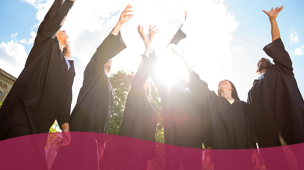 A group of high school graduates in their graduation robs toss their caps into the air